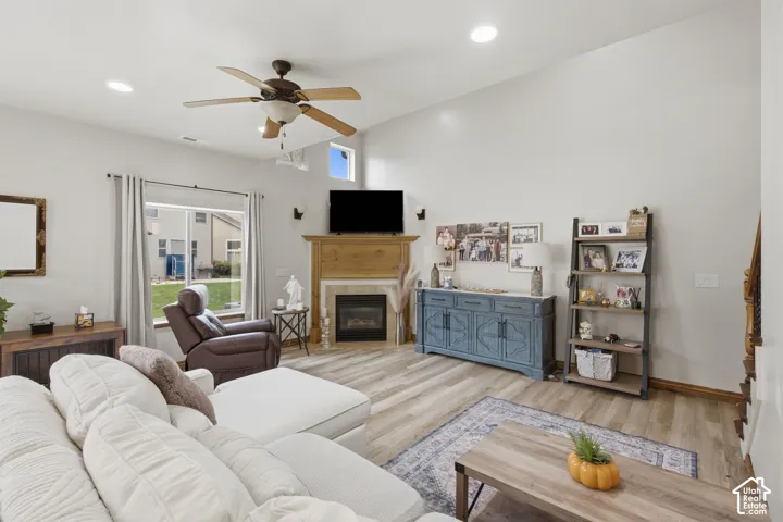 Vaulted ceilings featuring recessed lighting and a ceiling fan, complemented by wood-finish flooring and a corner fireplace with a prominent mantel