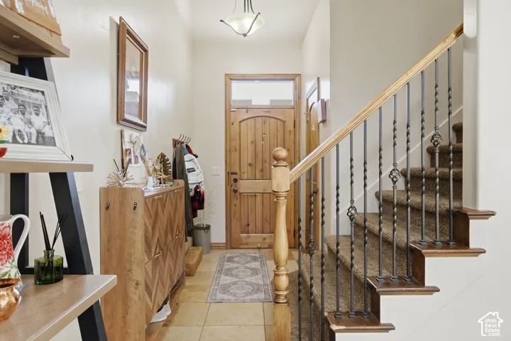 Entryway featuring tile flooring, a natural wood entry door with a transom window, and a staircase with decorative metal balusters, wood handrail, and a carved newel post