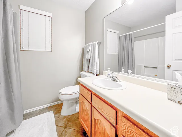 Bathroom featuring a solid-surface vanity countertop with an integrated oval sink, natural wood-finish cabinetry, large wall-mounted mirror, and tile flooring
