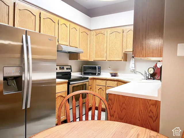 Kitchen featuring light-tone wood cabinetry, solid-surface countertops, and stainless steel appliances including a refrigerator and range