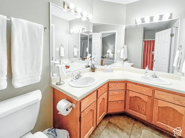 Corner vanity featuring wood cabinetry, dual oval drop-in sinks, a expansive wall-to-wall mirror, and overhead globe lighting fixtures
