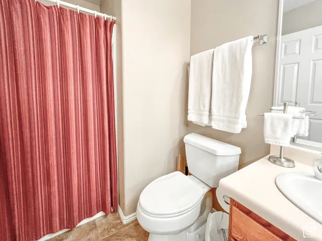 Bathroom featuring a wood-finish vanity with a molded countertop and integrated sink, complemented by neutral tile flooring and brushed-nickel hardware
