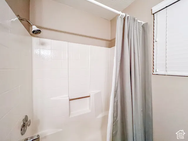 Tub and shower combination with white tile surround, integrated shelf, chrome plumbing fixtures, and horizontal window blinds