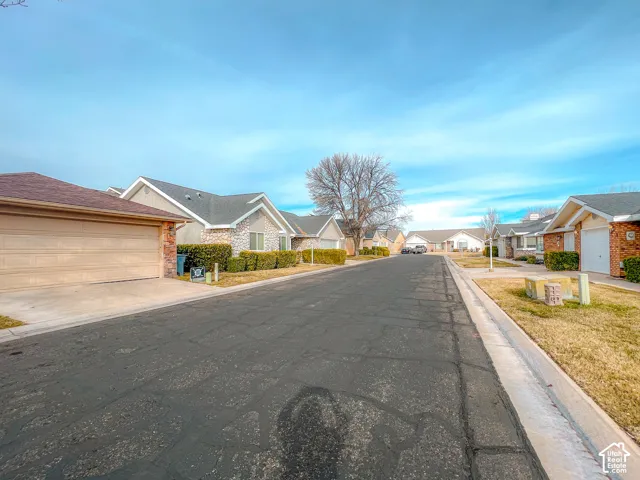 Residential streetscape featuring asphalt paving, concrete curbing, and single-story structures with composite shingle roofing and masonry accents