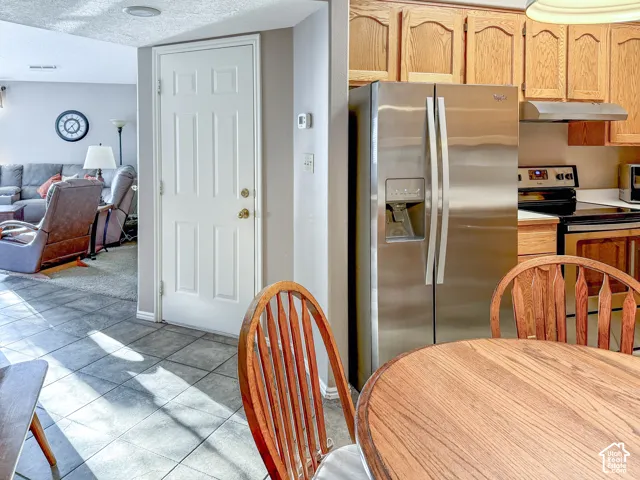 Kitchen area featuring natural wood cabinetry, stainless steel French-door refrigerator, integrated range, and tile flooring