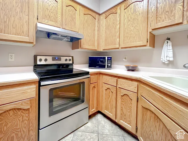 Kitchen featuring wood cabinetry, stainless steel range, stainless steel range hood, and tile flooring