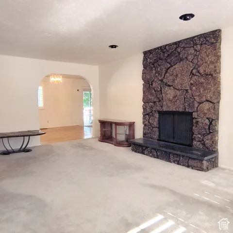 Floor-to-ceiling stone fireplace featuring a metal fire screen and a solid slab hearth, complemented by recessed lighting and a decorative arched entryway to dining