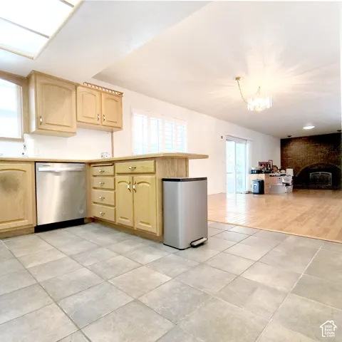 Kitchen featuring wood cabinetry, stainless steel dishwasher, tile flooring, and integrated lighting, opening to a space with a brick fireplace