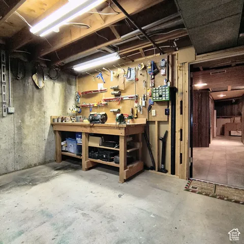 Built-in wooden workbench, wall-mounted pegboard organization system, concrete foundation walls, and fluorescent overhead lighting