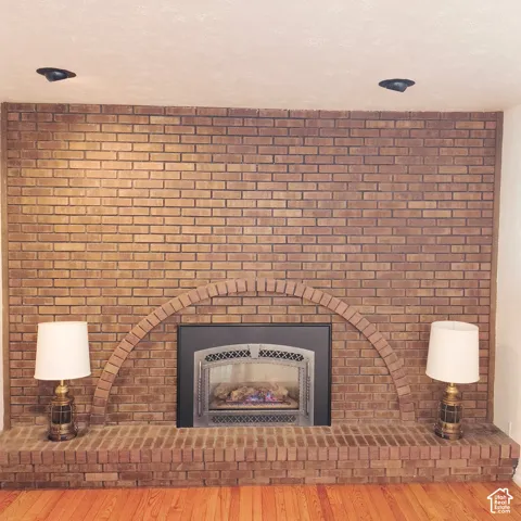 Full-height masonry brick fireplace surround featuring an arched brick detail, an elevated brick hearth, and an inset fireplace insert with black metal framing