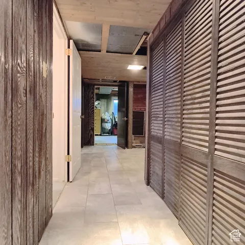 Hallway featuring large-format ceramic tile flooring, built-in louvered-style closet doors, and wood-paneled wall accents