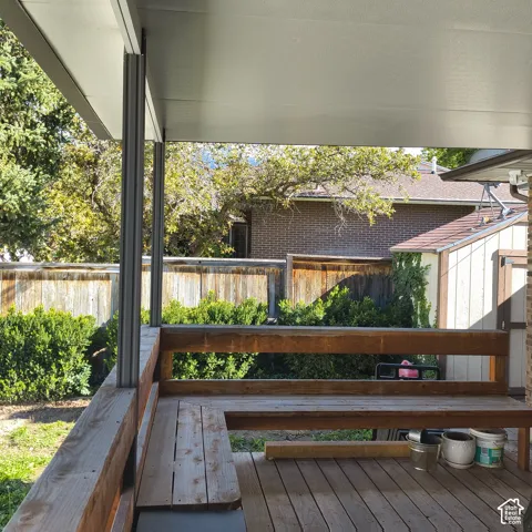 Covered wooden deck featuring a built-in L-shaped bench, a solid roof structure, and perimeter wood fencing