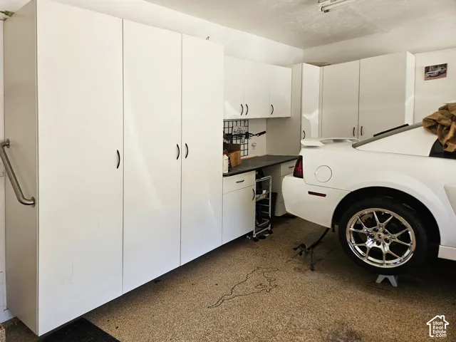 Garage storage area featuring floor-to-ceiling white cabinetry, integrated workbench, and speckled epoxy-finish flooring