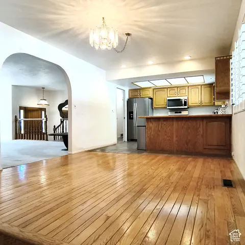 Dining area featuring wood-finish flooring, a decorative chandelier, an arched entryway, and a breakfast bar kitchen with wood cabinetry
