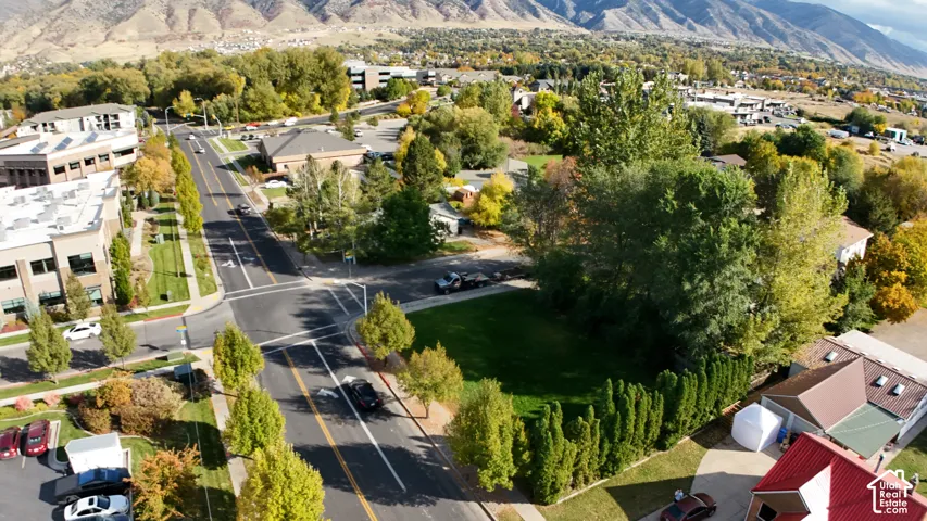 Aerial perspective of a corner lot featuring mature trees, manicured lawn, established landscaping, and mountain backdrop