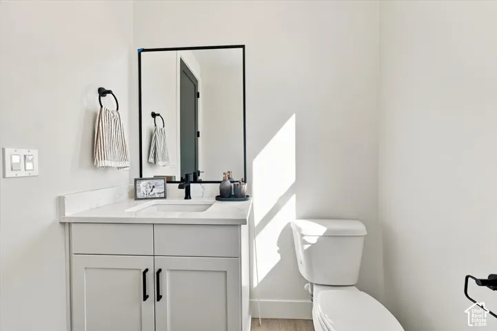Vanity featuring a stone-composite countertop, rectangular undermount sink, matte black faucet, and framed wall mirror, accompanied by a two-piece elongated toilet