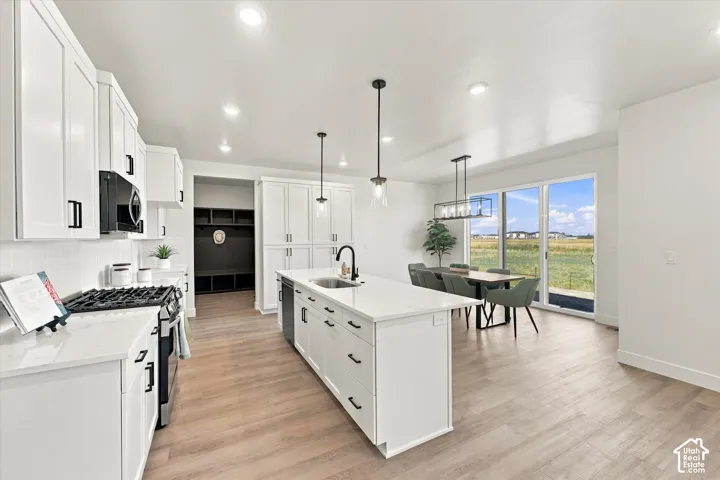 Kitchen featuring white cabinetry, quartz countertops, a central island with an undermount sink, wood-finish flooring, and sliding glass doors