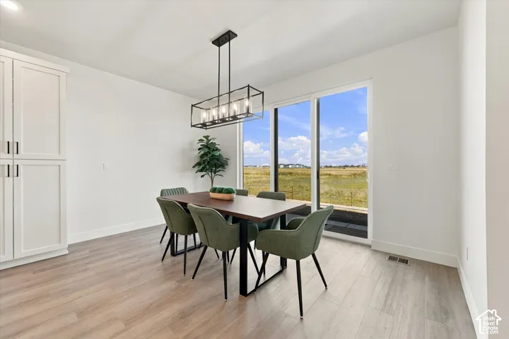 Dining area featuring wood-finish flooring, floor-to-ceiling built-in cabinetry, an open-frame rectangular chandelier, and glass sliding doors revealing a landscape backdrop
