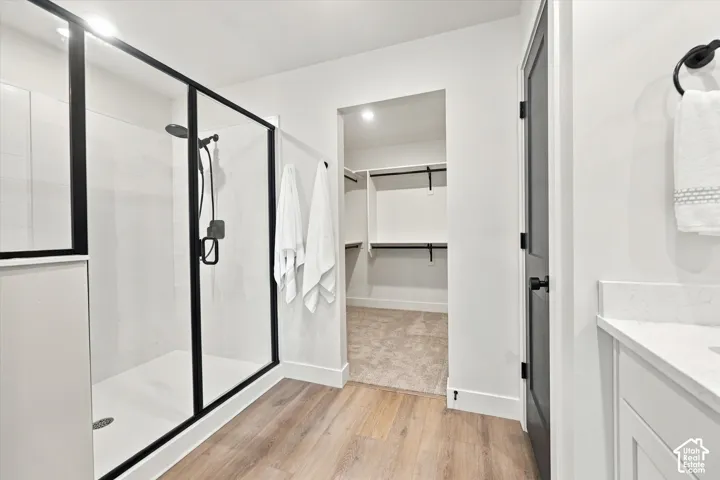 Walk-in shower with matte black fixtures and glass enclosure, wood-finish flooring, white vanity with quartz countertop, and built-in closet shelving