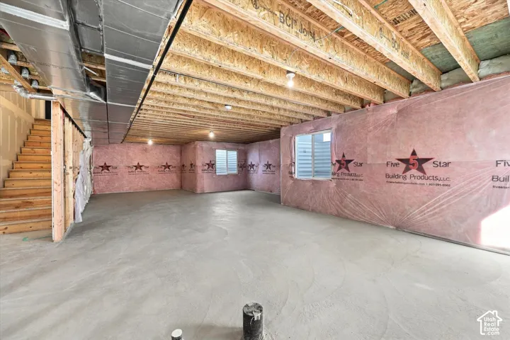 Unfinished lower level featuring exposed wood joist ceilings, concrete flooring, exposed wall insulation, two egress windows, and a staircase