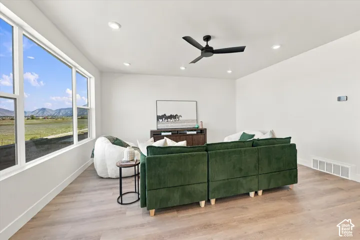 Large picture windows featuring mountain scenery, wood-finish flooring, matte black ceiling fan, and recessed lighting