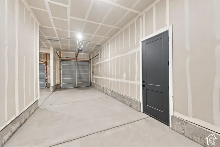 Garage featuring concrete flooring, a paneled metal garage door, and a solid-core charcoal entry door