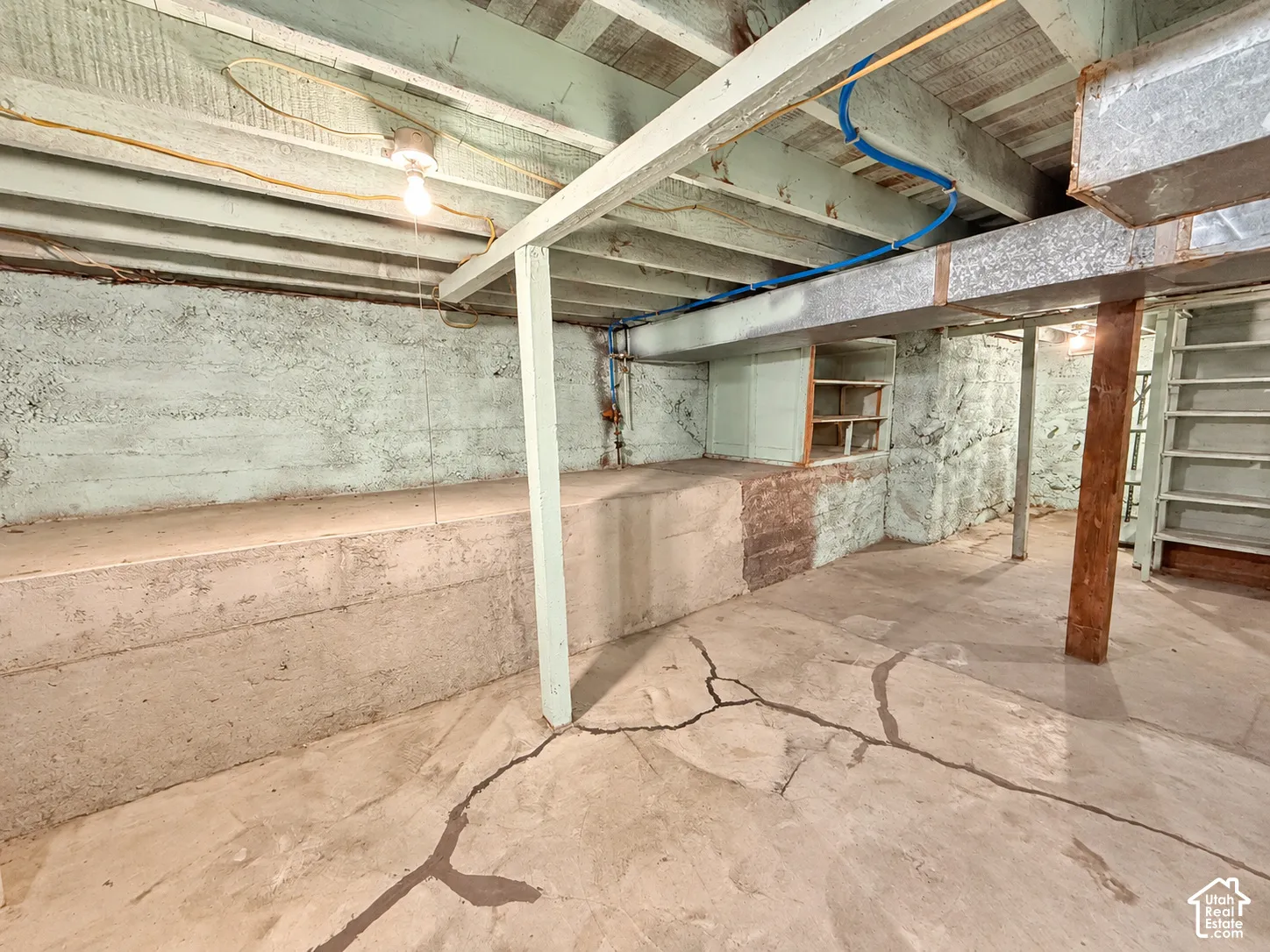 Unfinished storage area featuring concrete foundation walls, exposed wood ceiling joists, built-in wooden shelving, and a concrete floor