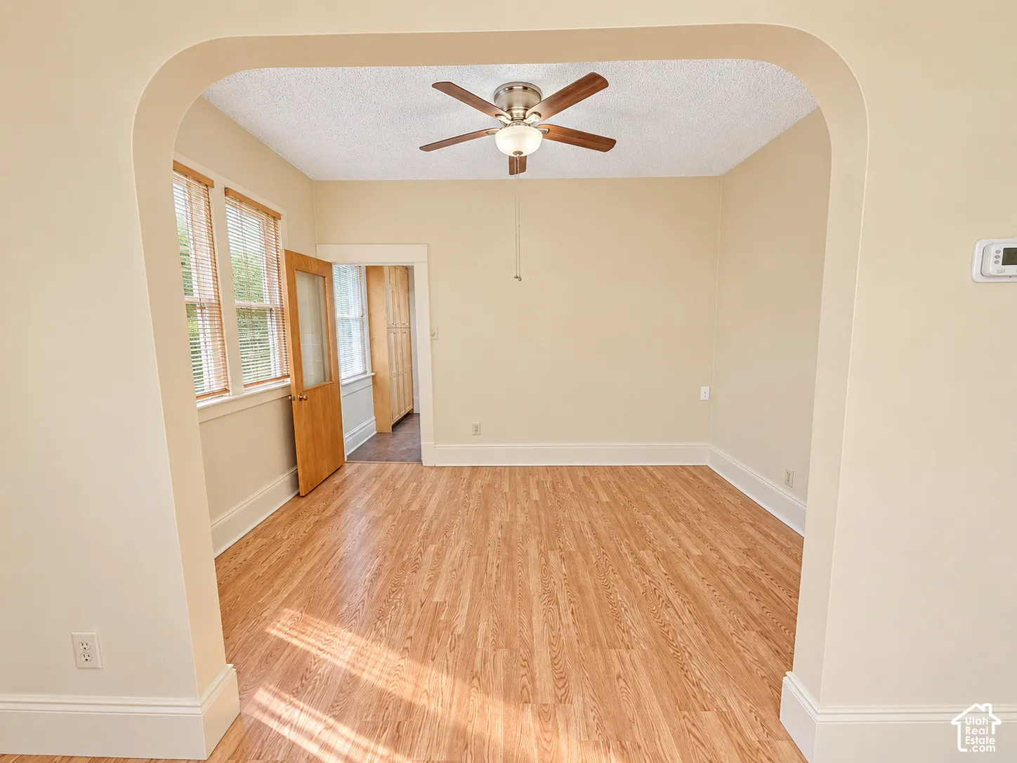 Arched entryway featuring wood-finish flooring, a ceiling fan with integrated lighting, and natural wood-trim door