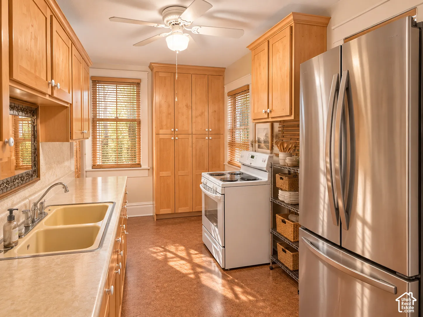 Kitchen featuring custom wood cabinetry, floor-to-ceiling pantry storage, neutral laminate countertops, a dual-basin sink, and stainless steel refrigerator