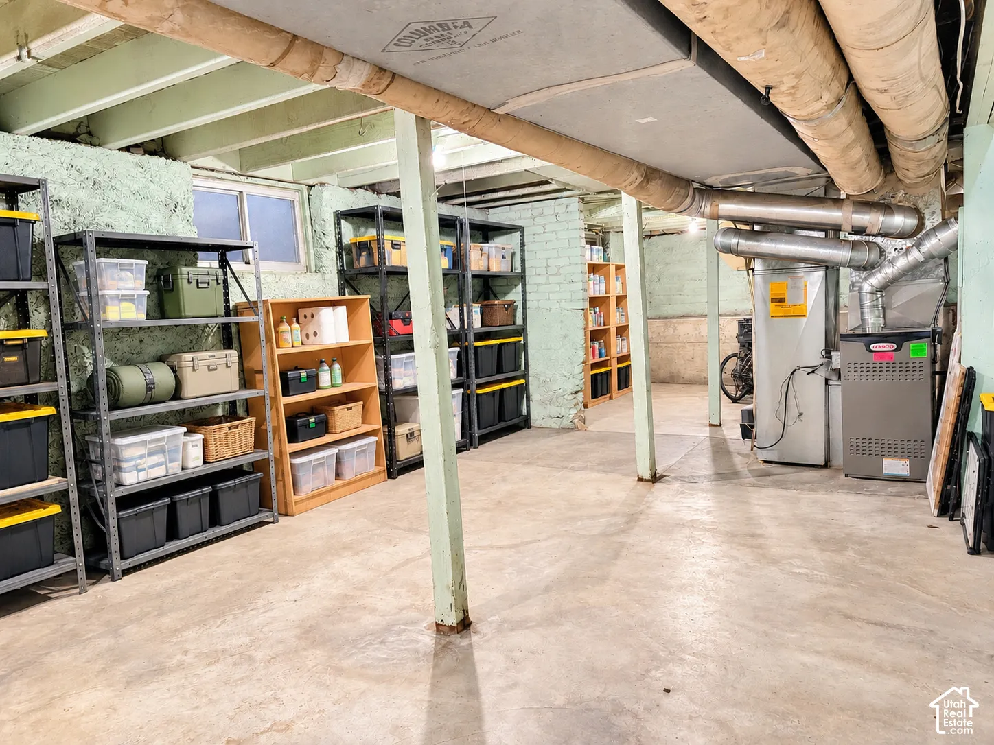 Unfinished lower level featuring a concrete floor, painted brick walls, exposed ceiling joists, and a metal furnace system