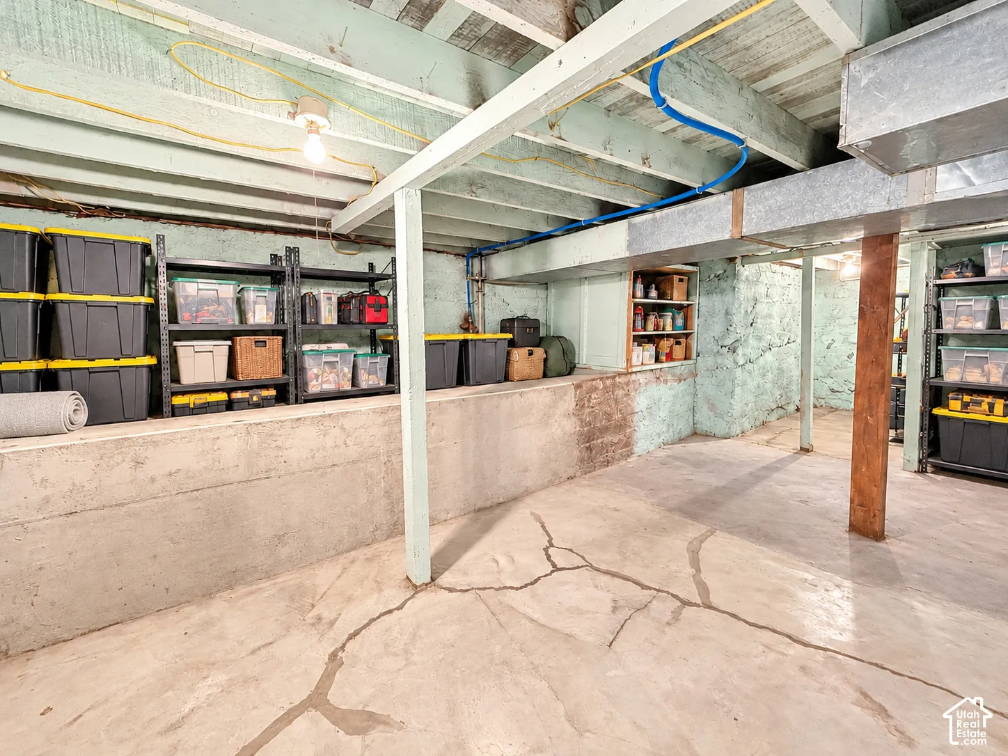 Unfinished lower level with concrete flooring, poured concrete foundation walls, exposed timber ceiling joists, and built-in wooden shelving