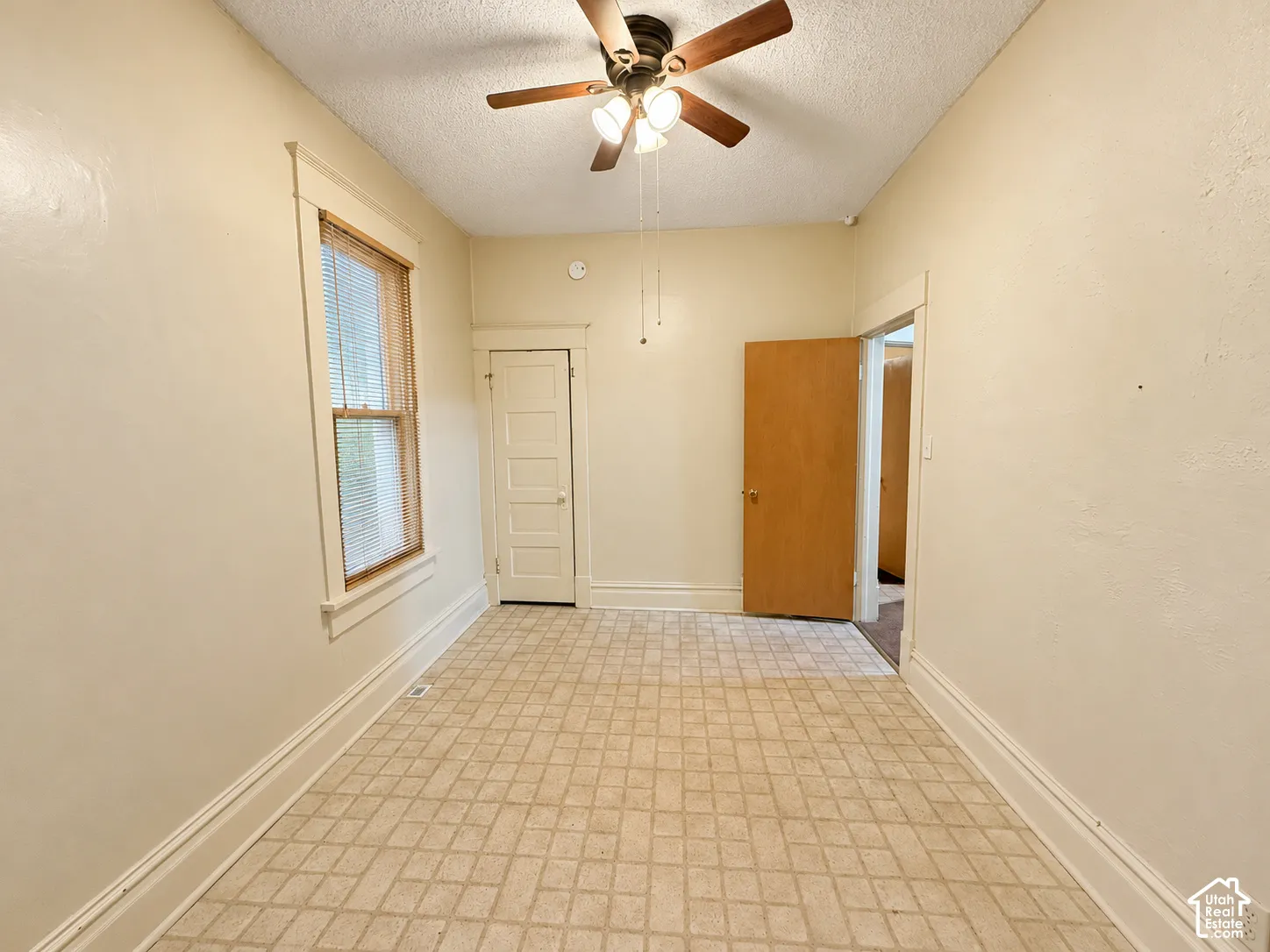 Neutral-toned room featuring a multi-light ceiling fan, grid-patterned tile flooring, a window with classic trim, and a paneled interior door