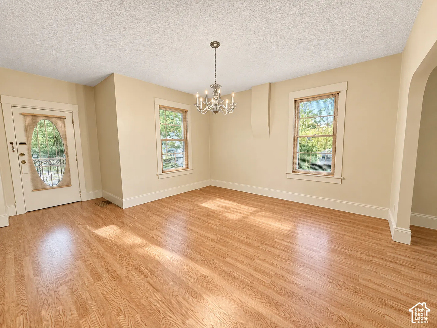 Hardwood flooring, multi-pane windows with casing, arched entryway, and traditional multi-light chandelier