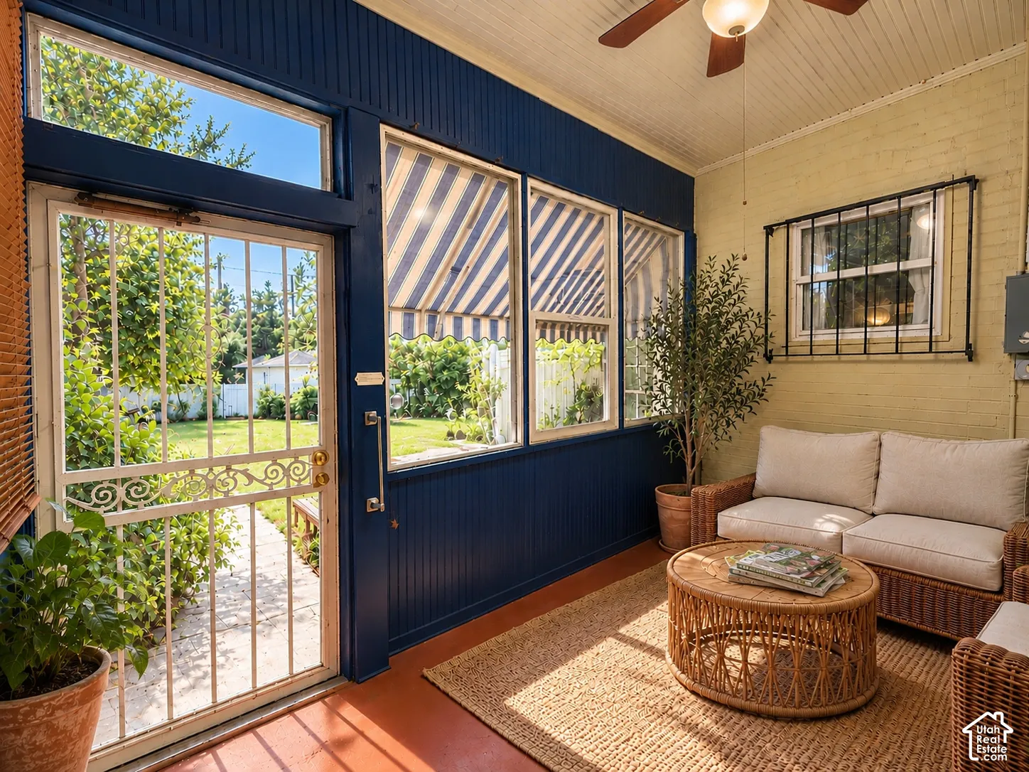 Enclosed sunroom featuring beadboard wall paneling, large windows with exterior striped awnings, and an ornate metal security door