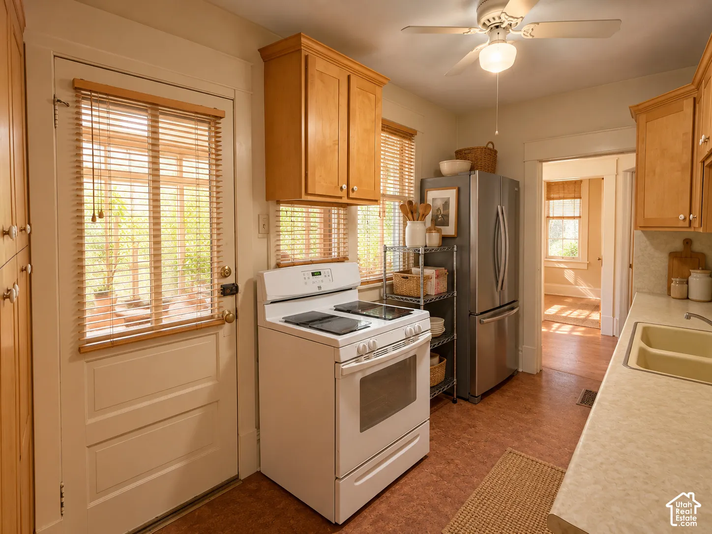 Kitchen featuring natural wood cabinetry, stainless steel refrigerator, white freestanding range, dual-basin sink, and a ceiling-mounted light fixture