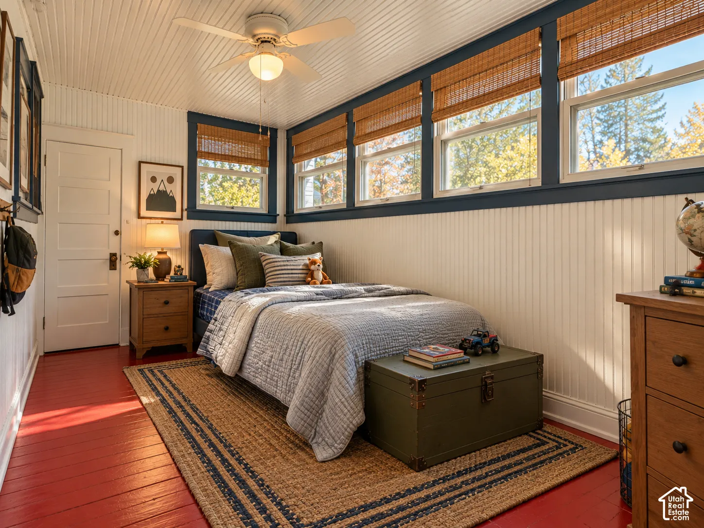 Beadboard wall paneling, ceiling-mounted paddle fan, multi-pane windows with contrasting trim, and painted wood flooring