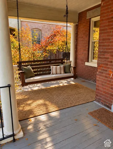 Covered front porch featuring red brick siding, classic white columns, and wood-plank flooring