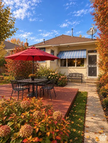 Rear exterior featuring a raised wood-finish deck, concrete paver walkway, retractable striped fabric awning, and mature landscape plantings