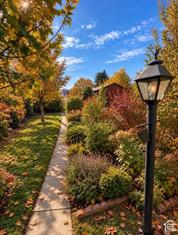 Landscaped grounds featuring a stone pathway, mature trees, perennial garden beds, and a decorative post lamp