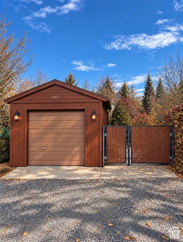 Detached garage featuring wood-paneled siding, a sectional garage door, dual wall-mounted exterior light fixtures, and a side-hinged privacy gate