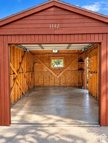 Detached garage featuring a concrete floor, exposed wood-frame wall construction, a single window, and a built-in corner shelf
