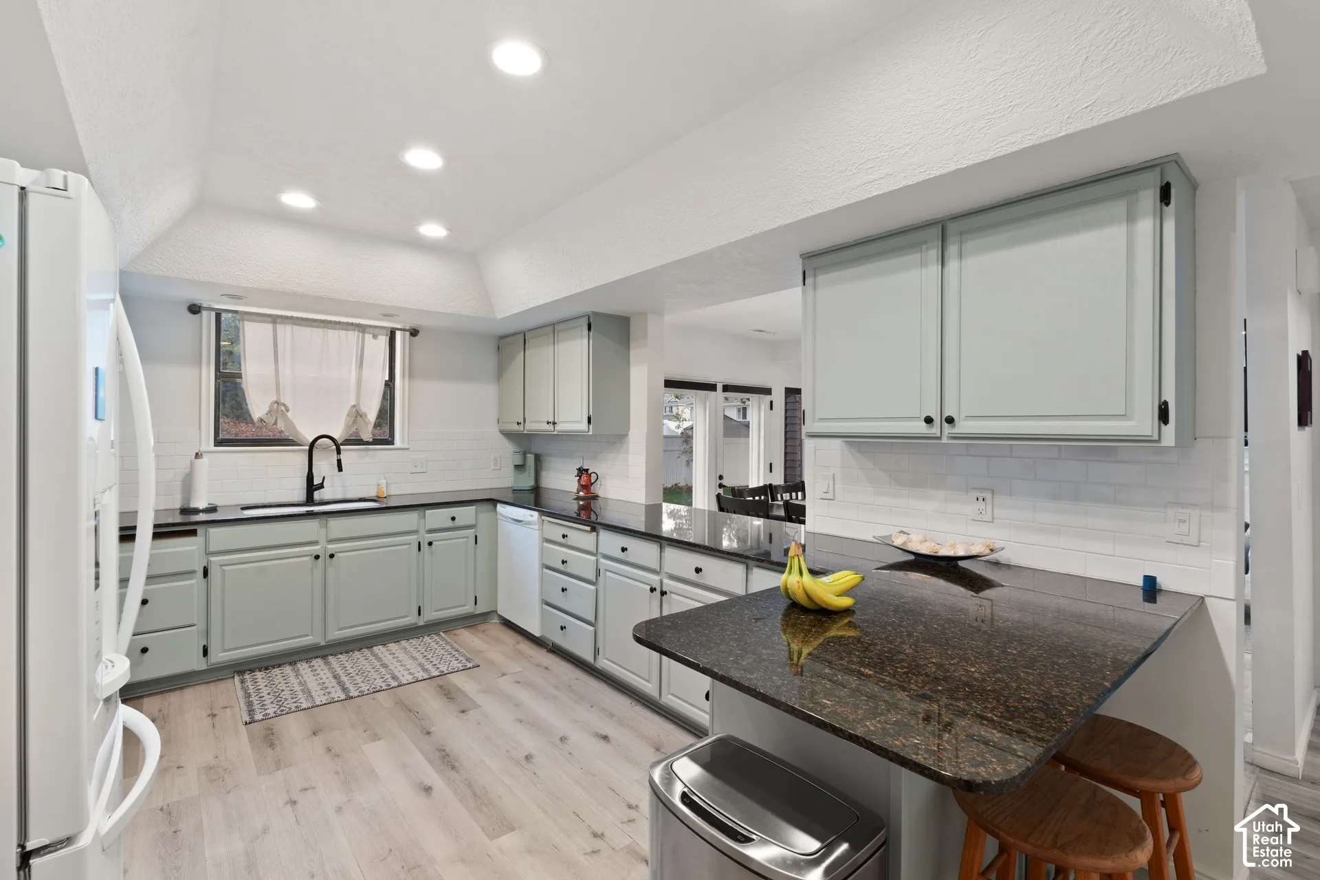 Kitchen featuring light-toned cabinetry, dark stone countertops, wood-finish flooring, recessed lighting, and white subway tile backsplash