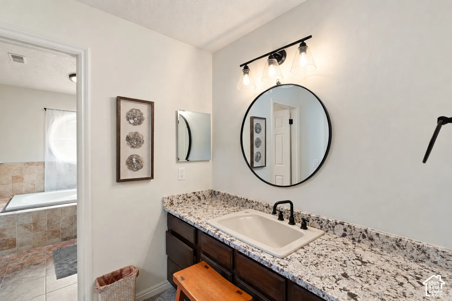 Vanity featuring a dark-finish wood cabinet, speckled stone-pattern countertop, integrated sink, matte black faucet, and circular wall-mounted mirror