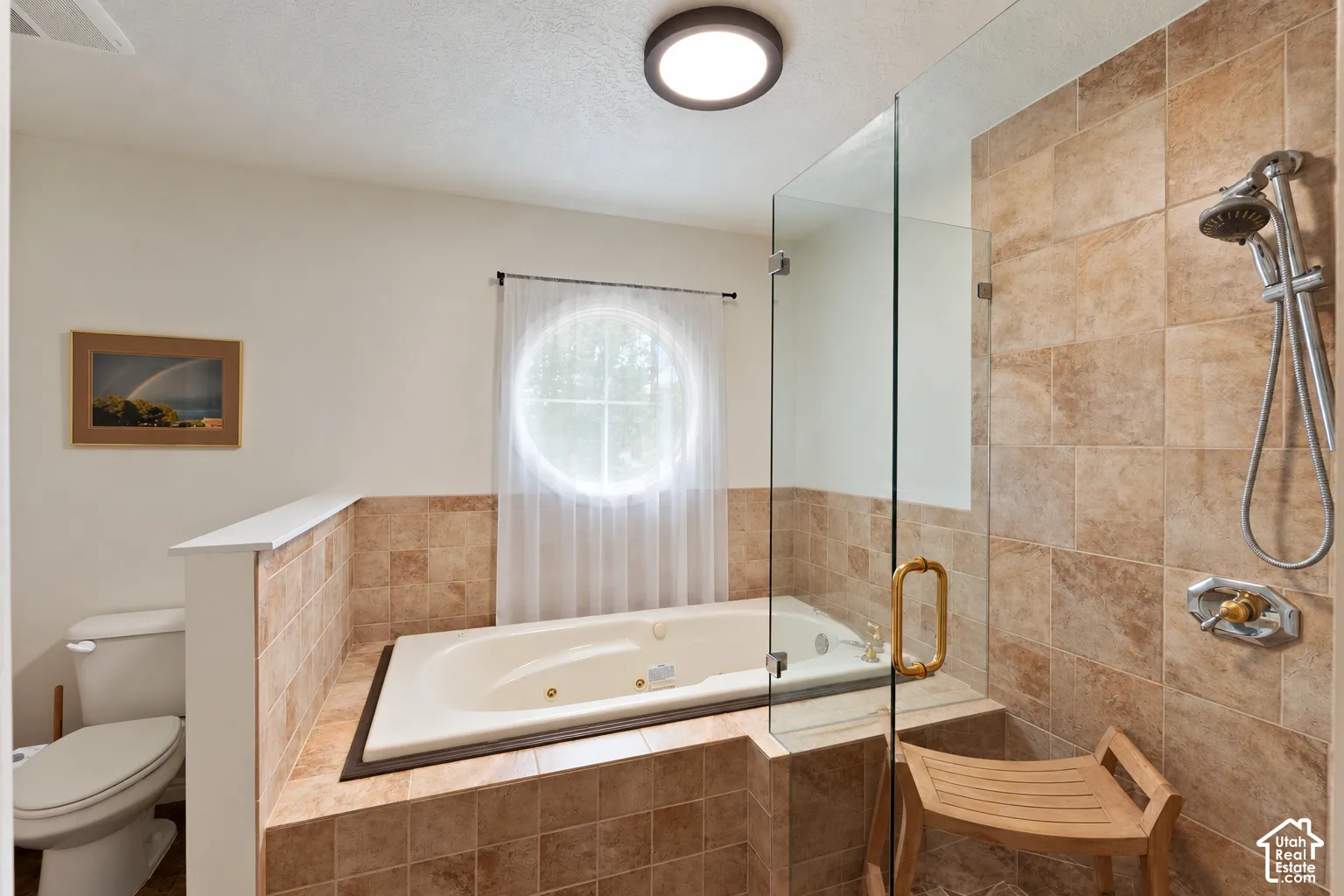 Jetted soaking tub and walk-in shower with stone-tile surround, glass enclosure, handheld shower fixture, and circular window