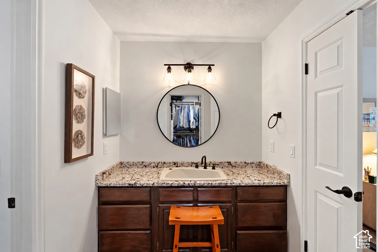 Dark wood cabinetry, stone-finish countertop, integrated basin, matte black faucet, and circular wall-mounted mirror
