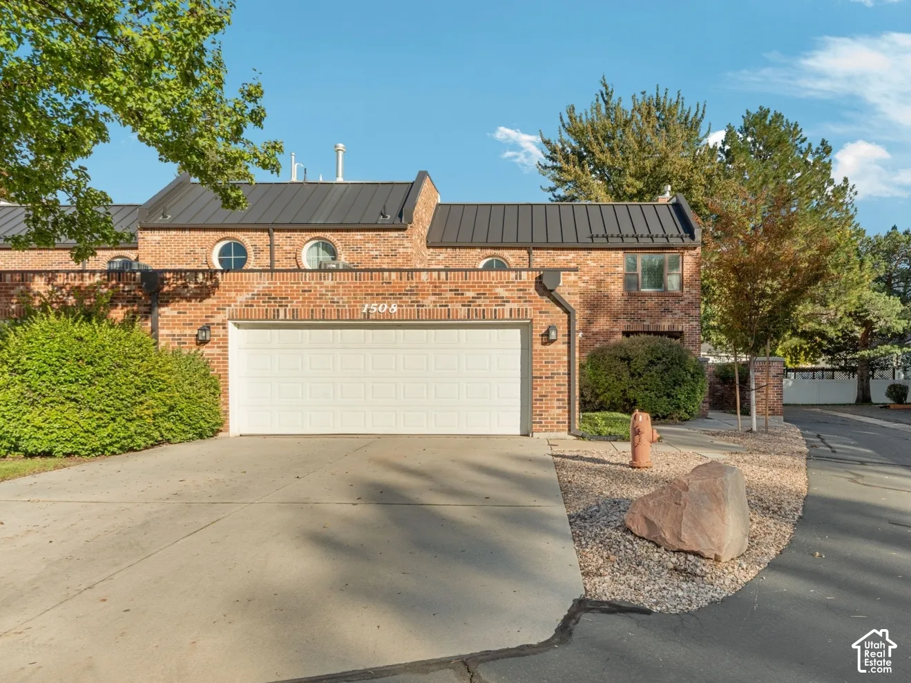 Brick exterior featuring a standing-seam metal roof, circular accent windows, and a multi-car garage with white sectional doors