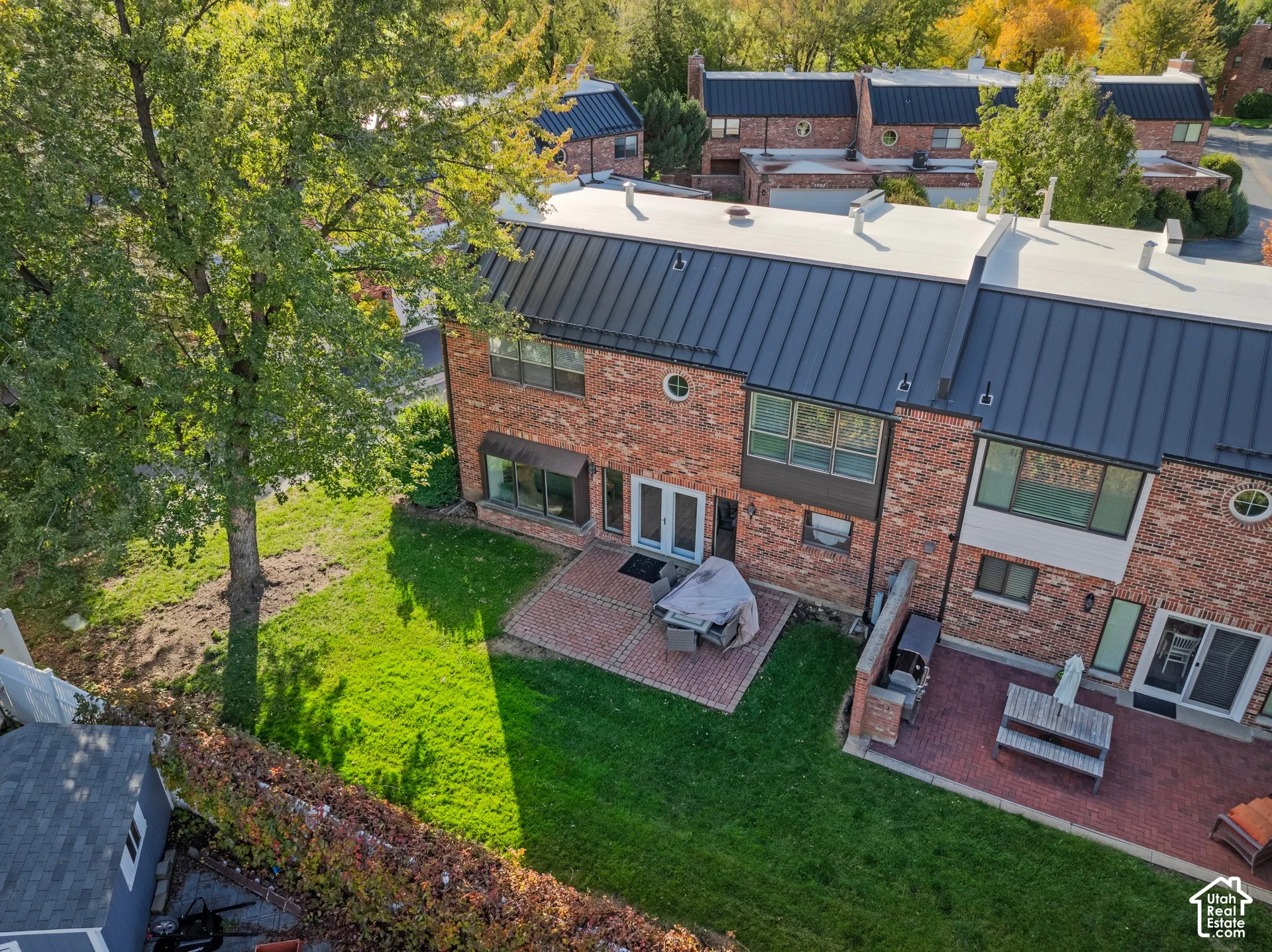 Brick exterior with a standing-seam metal roof, rear patio featuring paved brickwork, and mature landscaping