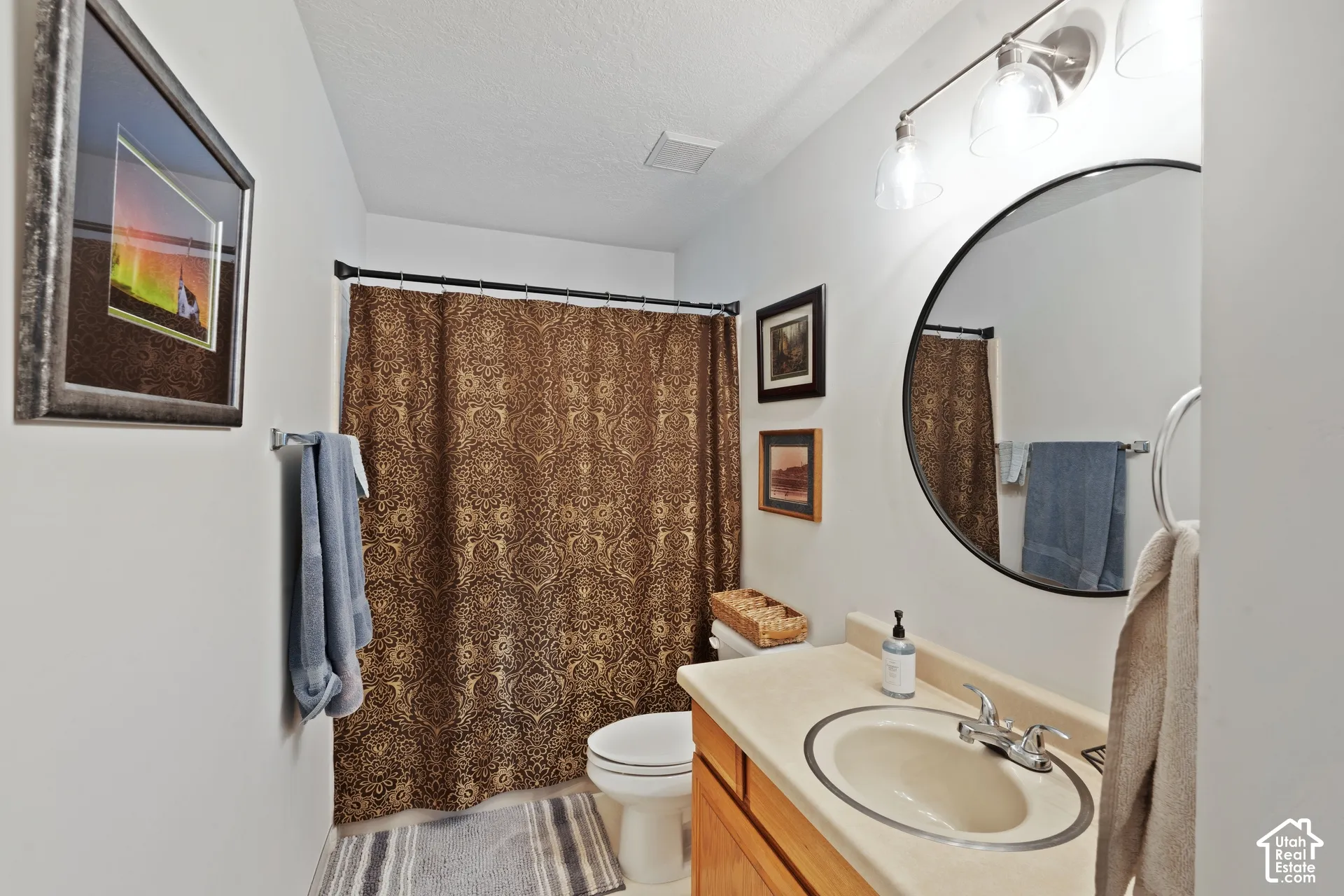 Bathroom featuring a vanity with an integrated basin, a round wall-mounted mirror, and a three-light fixture