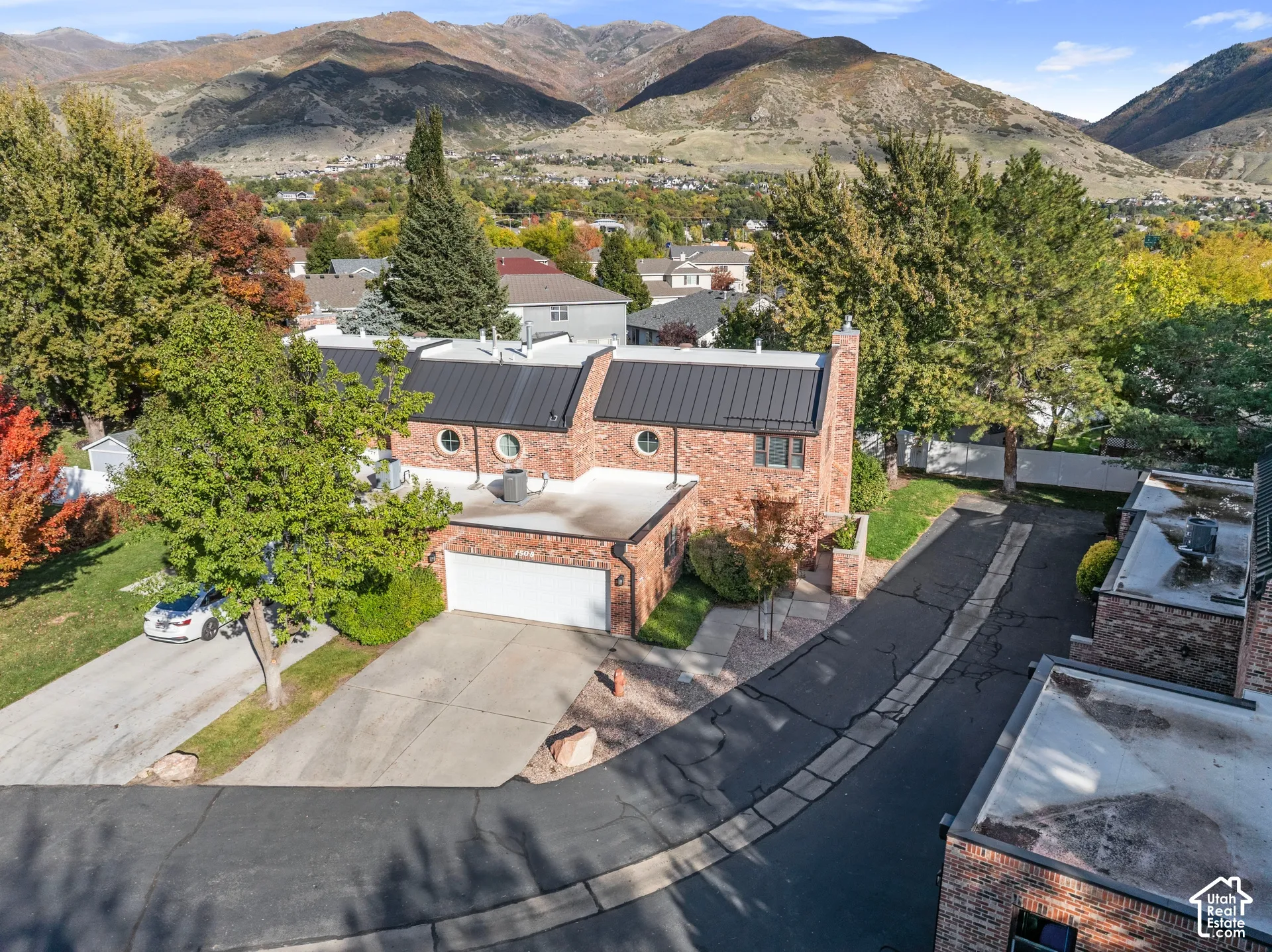 Brick exterior featuring a metal roof, circular accent windows, and a paved driveway with an attached two-car garage, set against a backdrop of mountain scenery