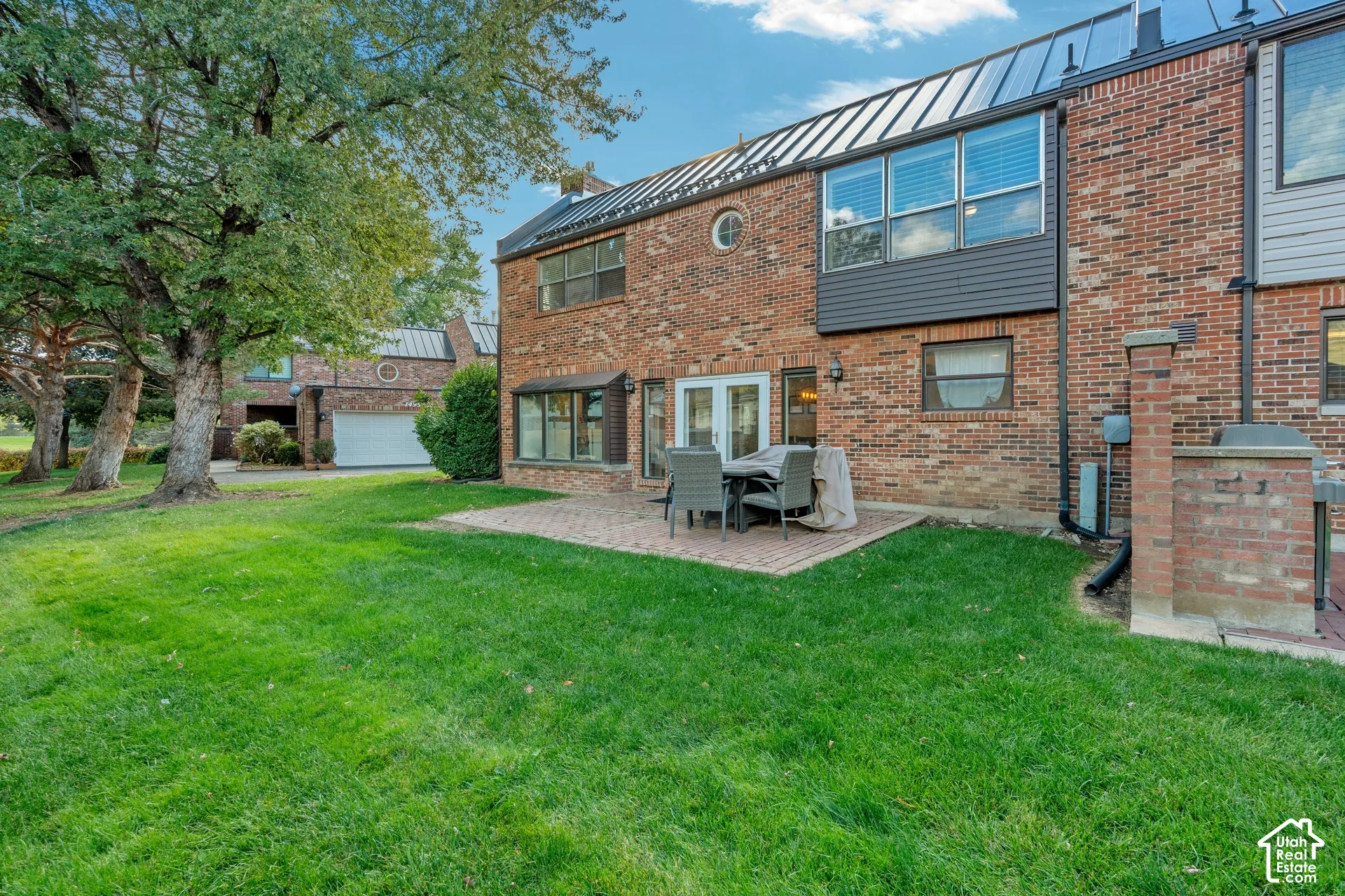 Exterior featuring a brick facade, standing seam metal roof, brick patio, and expansive lawn